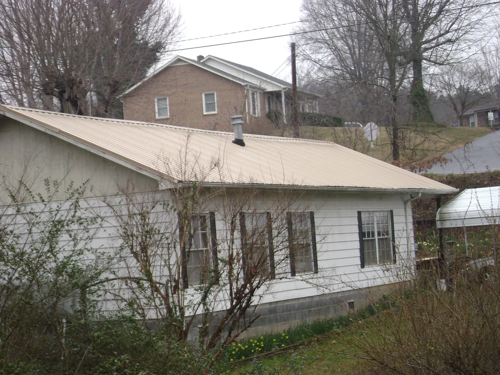 Tan metal roof on a white sided house set into a hillside — Commercial Roofing by Roofing Brothers in Orient